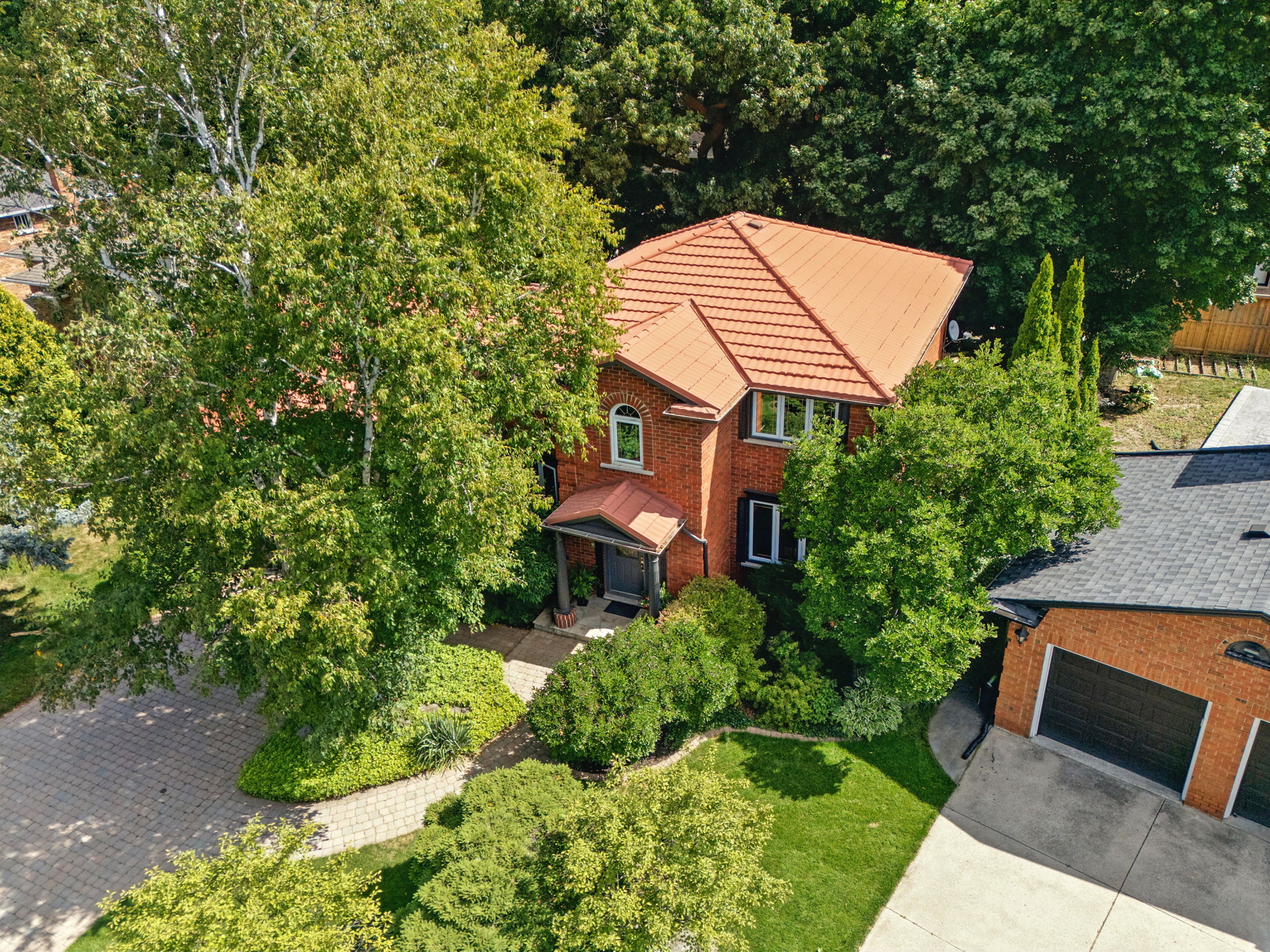 Aerial view of a red-brick home surrounded by mature trees and landscaped gardens